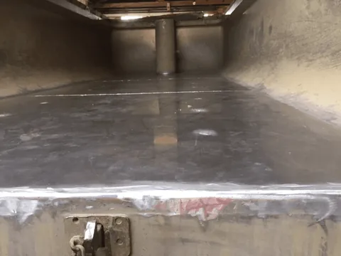 Inside a steel truck bin, looking along the floor to the front wall, with a fresh weld seam running across the rear edge