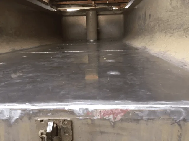 Inside a steel truck bin, looking along the floor to the front wall, with a fresh weld seam running across the rear edge